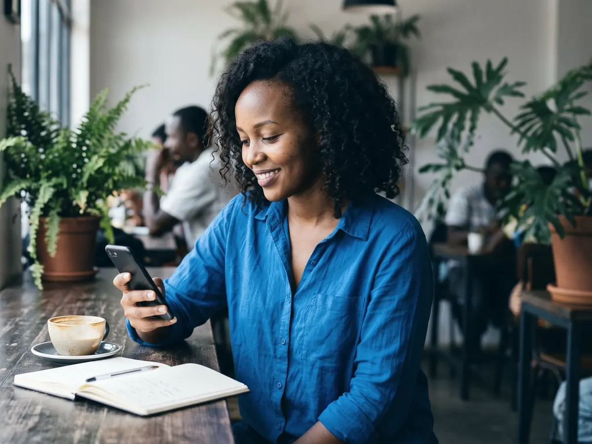 A woman smiles at her phone by a café window